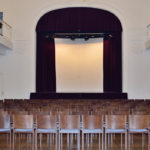 Jugenstilsaal mit Bestuhlung und Blick zur Bühne mit roten Samtvorhang
