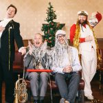 4 Männer mit Lametta und einem Weihnachtsbaum im Hintergrund