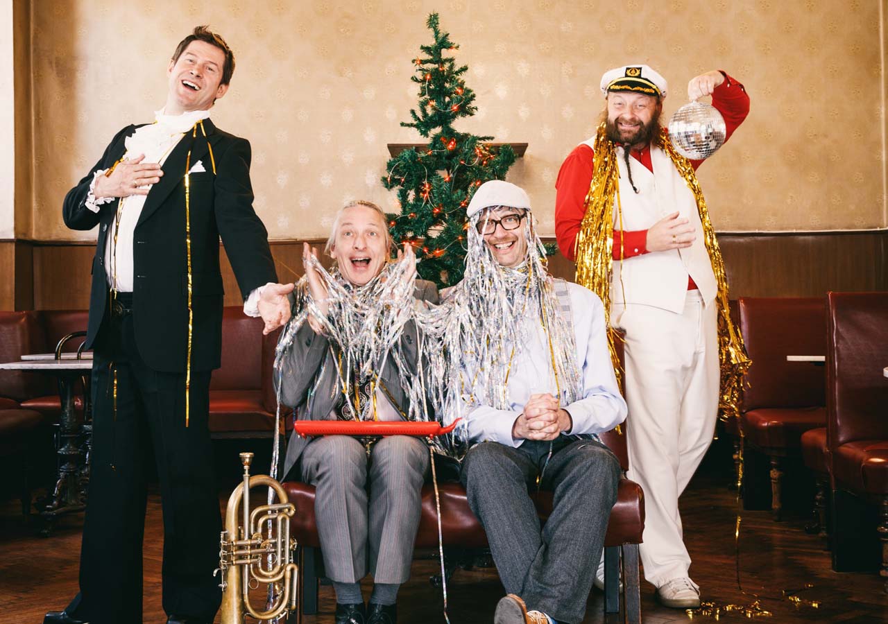 4 Männer mit Lametta und einem Weihnachtsbaum im Hintergrund